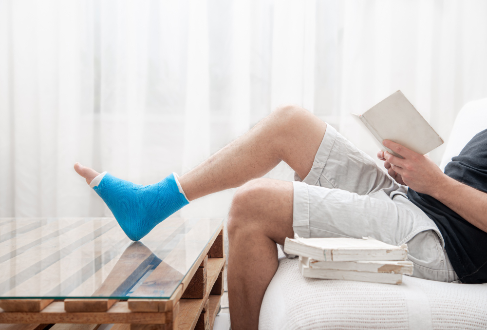 man with broken leg cast reads books against light background interior room